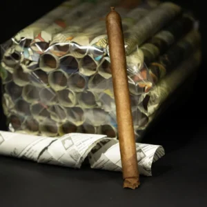 A single brown cigar stands upright in front of a large bundle of cigarettes wrapped in plastic on a dark surface.