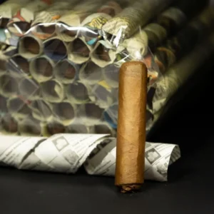 A brown cigar standing upright on a black surface with a bundle of rolled newspapers wrapped in plastic behind it.