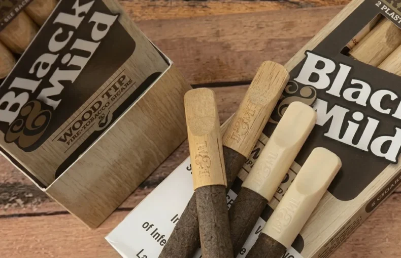 Assorted Black & Mild cigars in wooden packaging on a rustic table surface.